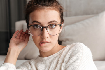 Image of lovely young woman in eyeglasses resting on sofa at home