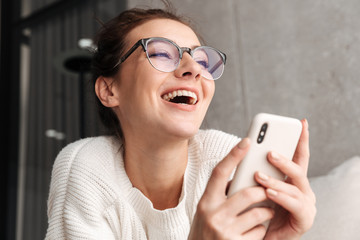 Image of woman in eyeglasses smiling and holding cellphone at home