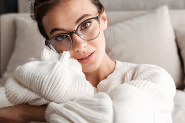 Image of lovely young woman in eyeglasses resting on sofa at home
