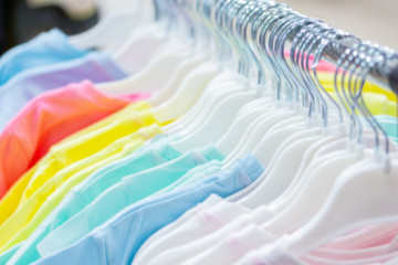 Defocus background wallpaper backdrop bokeh, summer clothes hanging on hangers in a store. cotton natural t-shirts white pink green blue.