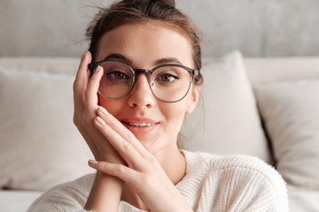 Image of lovely young woman in eyeglasses resting on sofa at home