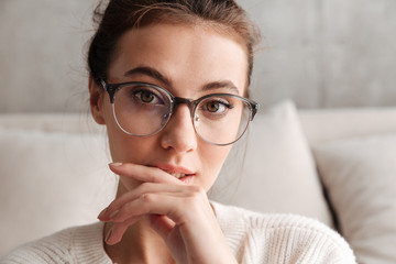 Image of lovely young woman in eyeglasses resting on sofa at home