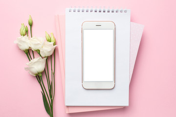 Mobile phone, white flower and notebook on pink background. Women's business technology composition