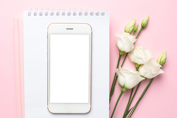Mobile phone, white eustoma flower and notebook on pink background.Women's business technology composition