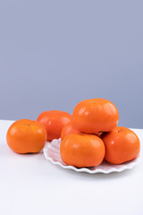 Fresh beautiful sliced sweet persimmon kaki isolated on white kitchen table with gray blue background, Chinese lunar new year design concept, close up.