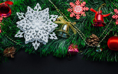 Christmas wreath decorated with a white snowflake, cones, red ball, red snowflake and beads on a black background