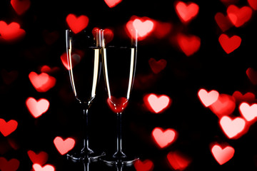 Fototapeta na wymiar Champagne glasses with bokeh heart lights on black background, New Year and Valentine day background