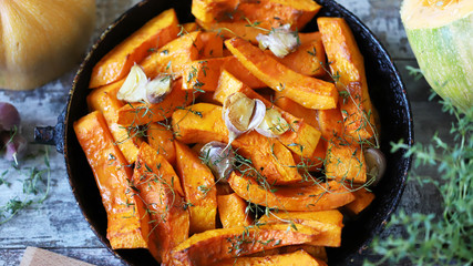 Baked pumpkin slices in a pan with herbs and garlic. Autumn lunch. Vegan food. Healthy snack.