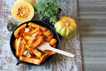 Baked pumpkin slices in a pan with herbs and garlic. Autumn lunch. Vegan food. Healthy snack.