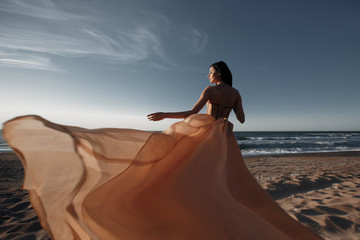 Fototapeta na wymiar Girl in a light dress on the beach at sunrise.beautiful women in a light pink dress walking along the beach at dawn.Good morning and relaxation.Young beautiful girl standing on a sandy beach in a ligh