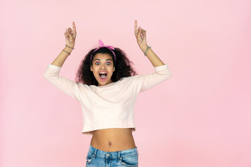 Amazed shocked young african american woman point fingers upward at copy space look at camera,...