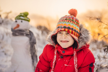 Cute boy in red winter clothes builds a snowman. Winter Fun Outdoor Concept