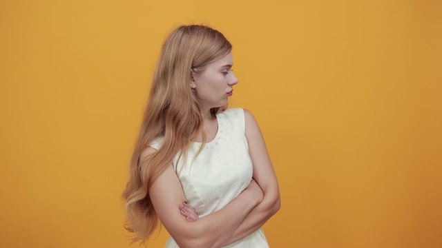 Disappointed caucasian blonde young woman keeping hands crossed, puffed out her cheeks over isolated orange background wearing white shirt. Lifestyle concept
