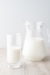 A glass and a jug of milk on a wooden table on a white background