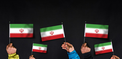 Fototapeta na wymiar Hands holds flags of Iran on dark background