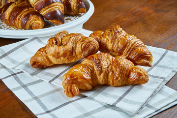 Three freshly baked croissants on beige fabric on a wooden background. Food photography for bakery cafes. Close up view.