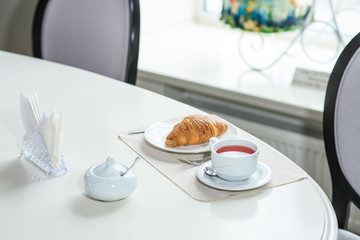 Fruit tea and delicious fresh croissant on the table in a cozy coffee shop