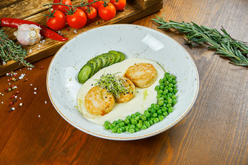 Fried chicken meatballs (cutlets) garnished with peas, mashed potatoes and cucumber in a white bowl on a wooden background. Tasty and healthy diet food. Close up view.