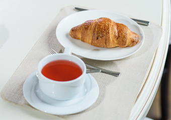 Fruit tea and delicious fresh croissant on the table in a cozy coffee shop