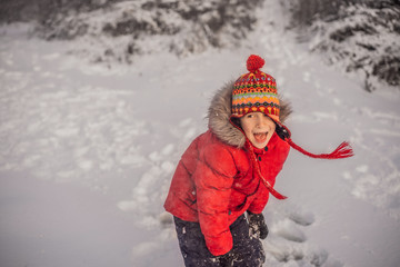 Boy in red fashion clothes playing outdoors. Active leisure with children in winter on cold days. Boy having fun with first snow. Happy little kid is playing in snow, good winter weather