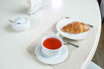 Fruit tea and delicious fresh croissant on the table in a cozy coffee shop