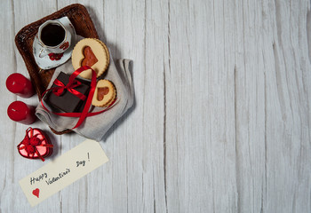 The Concept Of Valentine's Day. Beautiful Cup with hot black coffee, cookies in the form of hearts, chocolate, candles and decorative gift box in the form of a heart on a light wooden background.