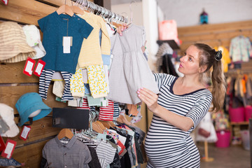 Pregnant woman examines a dress for a child in a store