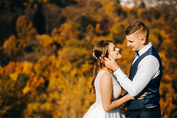 Lovely young couple in wedding clothes standing on a hill on city background