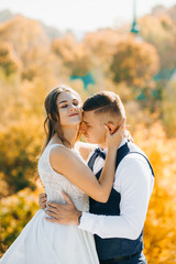Portrait of incredible newlyweds standing on a hill against the background of autumn forest.