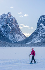 nice senior woman snowshoeing on a cold winter morning on the shore of Lago Dobbiaco, Three Peak Dolomites, South Tyrol, Italy