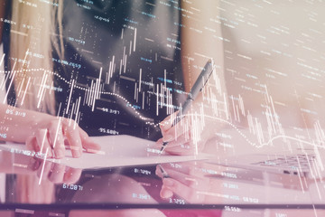 A woman hands writing information about stock market in notepad. Forex chart holograms in front. Concept of research. Double exposure