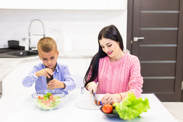 Small boy cutting in slices vegetables for salad with his mother in the kitchen. Family cooking background