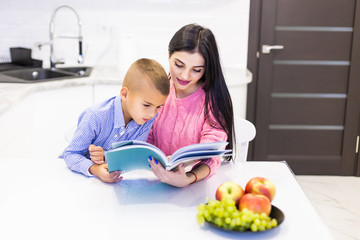 Young mother helping her son to do homework at home kitchen