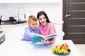 Young mother helping her son to do homework at home kitchen