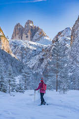 active senior woman snowshoeing in  spectacular Hoehlenstein Valley under the famous Three Peaks, Dolomites  near village of Toblach, South Tyrol, Italy