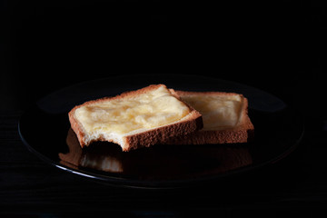 Two grilled toast with cheese on a black plate and a black background