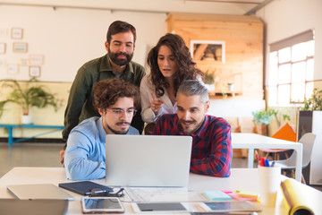 Focused coworkers in casual watching video presentation on laptop. Business colleagues in casual meeting in contemporary office space. Teamwork concept