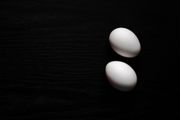 Two white chicken eggs on a black background close up