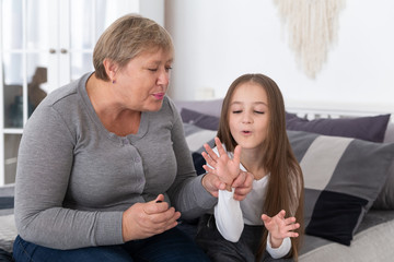 Grandmother and granddaughter are sitting on the bed and doing manicure, blow on nail polish. Happy...