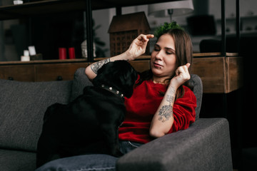 Naklejka premium Young woman playing with pug dog on sofa at home
