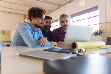 Team of developers using laptop together, watching content and talking. Business colleagues in casual meeting in contemporary office space. Brainstorming concept