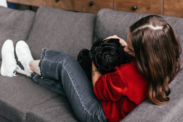 Selective focus of girl with leg prosthesis stroking pug on sofa
