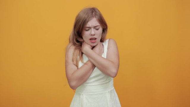 Charming caucasian blonde young woman keeping hands on neck, choking herself over isolated orange background wearing white shirt. Lifestyle concept