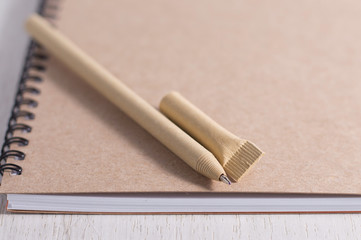 Brown pen and notebook made from recycled paper lie on a white wooden table The concept of environmental protection, save nature, ecology zero waste. No pollution land. To type notes, ideas.