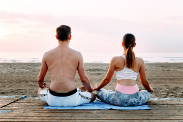 Fototapeta premium steamy yoga girl with a man on the beach near the ocean at dawn
