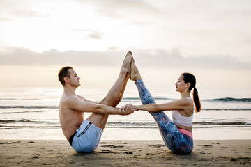 Acroyoga steamy yoga girl with a man on the beach near the ocean at dawn