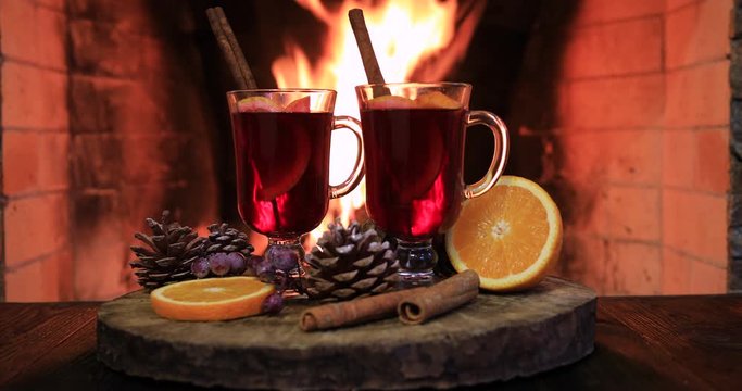 Two glasses of hot mulled wine with spices on wooden table against fireplace
