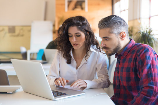 Serious Coworkers Discussing Project And Using Laptop Together. Business Colleagues In Casual Working Together In Contemporary Office Space. Partnership Or Consulting Concept