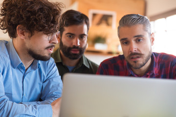 Team of coworkers watching and analyzing content on laptop screen together. Business colleagues in casual meeting in contemporary office space. Teamwork concept
