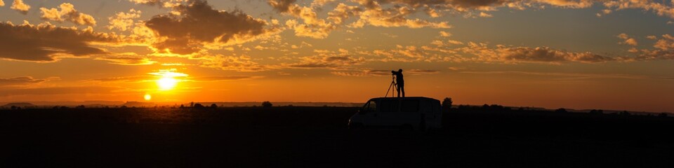 Fototapeta na wymiar Panoramic of a field sunset with photographer taking pictures on top of the van